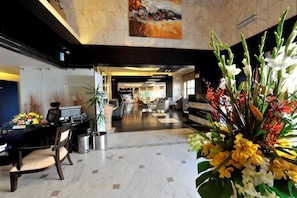 Hall d'hotel con reception, area salotto e un'ampia composizione floreale.