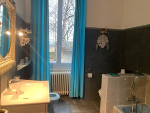 A bathroom with a sink, toilet, and shower. There is a window with curtains, a radiator, and a decorative wall piece. - La Gabetière (Estrablin)
