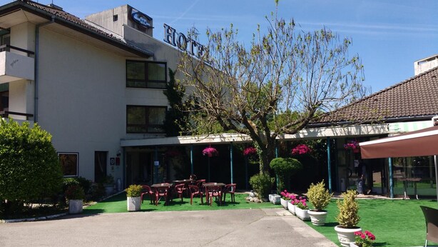 Un hotel con un área de estar al aire libre techada, un jardín con plantas en macetas y un cielo despejado.