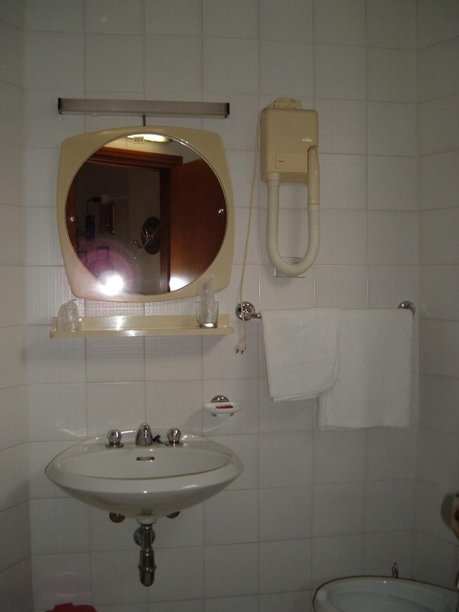 A bathroom with a sink, mirror, towel rack, and a toilet paper holder.