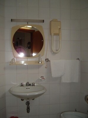 A bathroom with a sink, mirror, towel rack, and a toilet paper holder. - Albergo Luca (Ivrea)