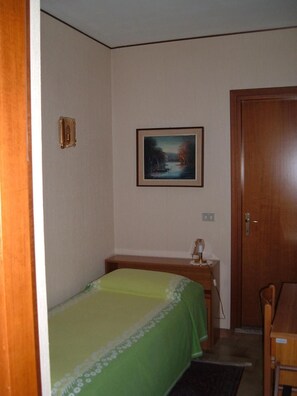 Una habitación pequeña y sencilla con cama, escritorio y puerta.