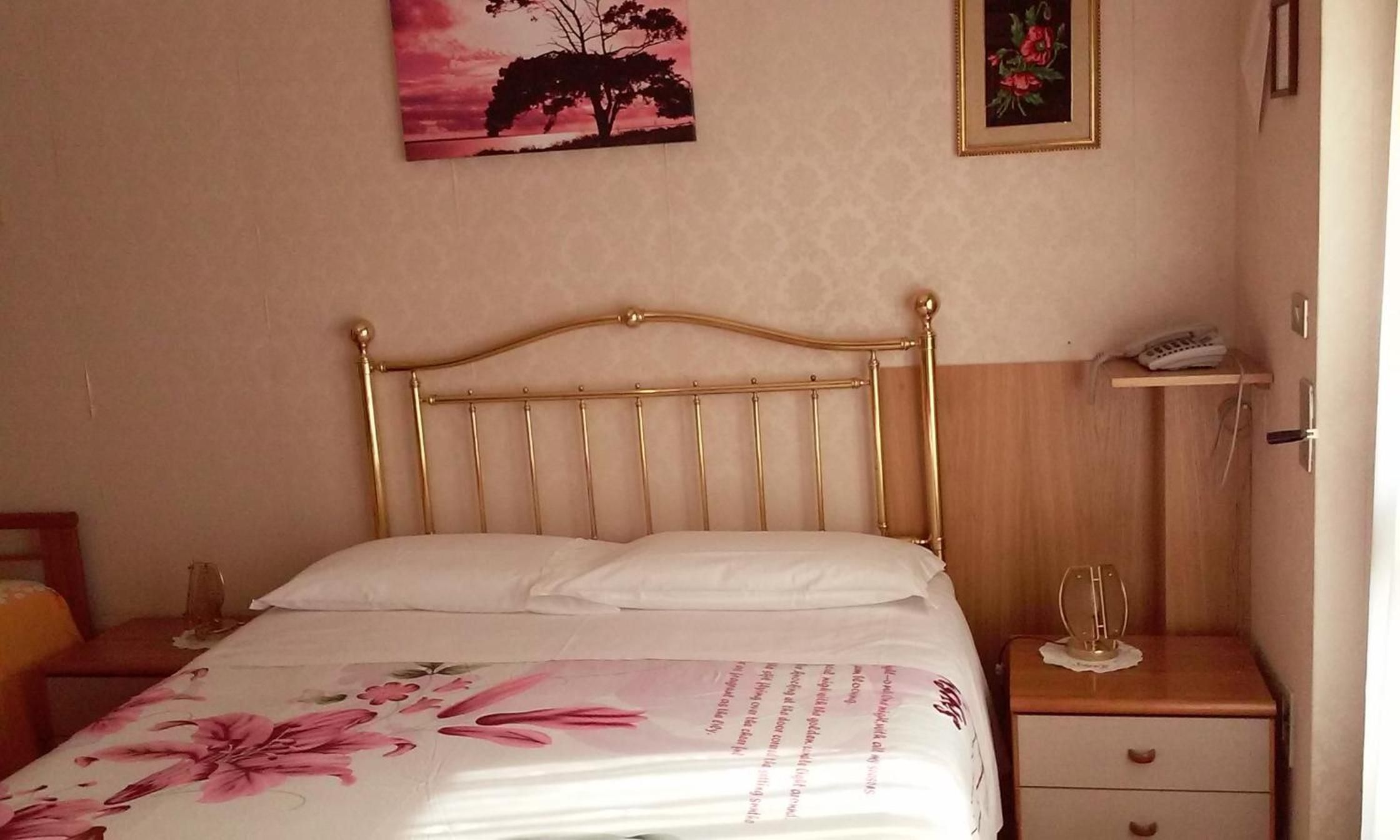 Un lit avec une tête de lit, une table de chevet avec une lampe et un mur orné de deux tableaux encadrés.