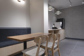 Ein modernes Interieur mit einem Holztisch und -stühlen, einer dunklen Bank und einer Küchenzeile mit einer Kaffeemaschine.