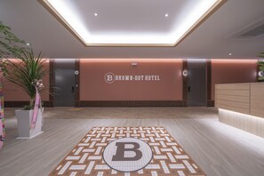 Ein Hotel-Empfangsbereich mit modernem Design, einer Rezeption und einem großen Buchstaben 'B' auf dem Boden.