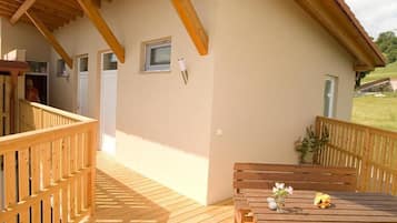 A wooden deck with a table and benches, a small window, and a door leading to an interior space.