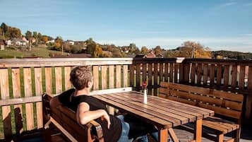 A person sitting on a wooden bench with a table in a deck area.