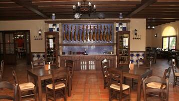 Interior de restaurante com mesas e cadeiras de madeira, piso ladrilhado e um painel na parede exibindo alimentos.