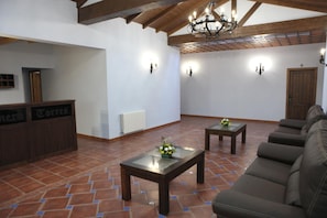 A spacious living area with a sofa, two tables, a reception desk, and a chandelier. - Hotel Rural Romero Torres (Fuente Obejuna)