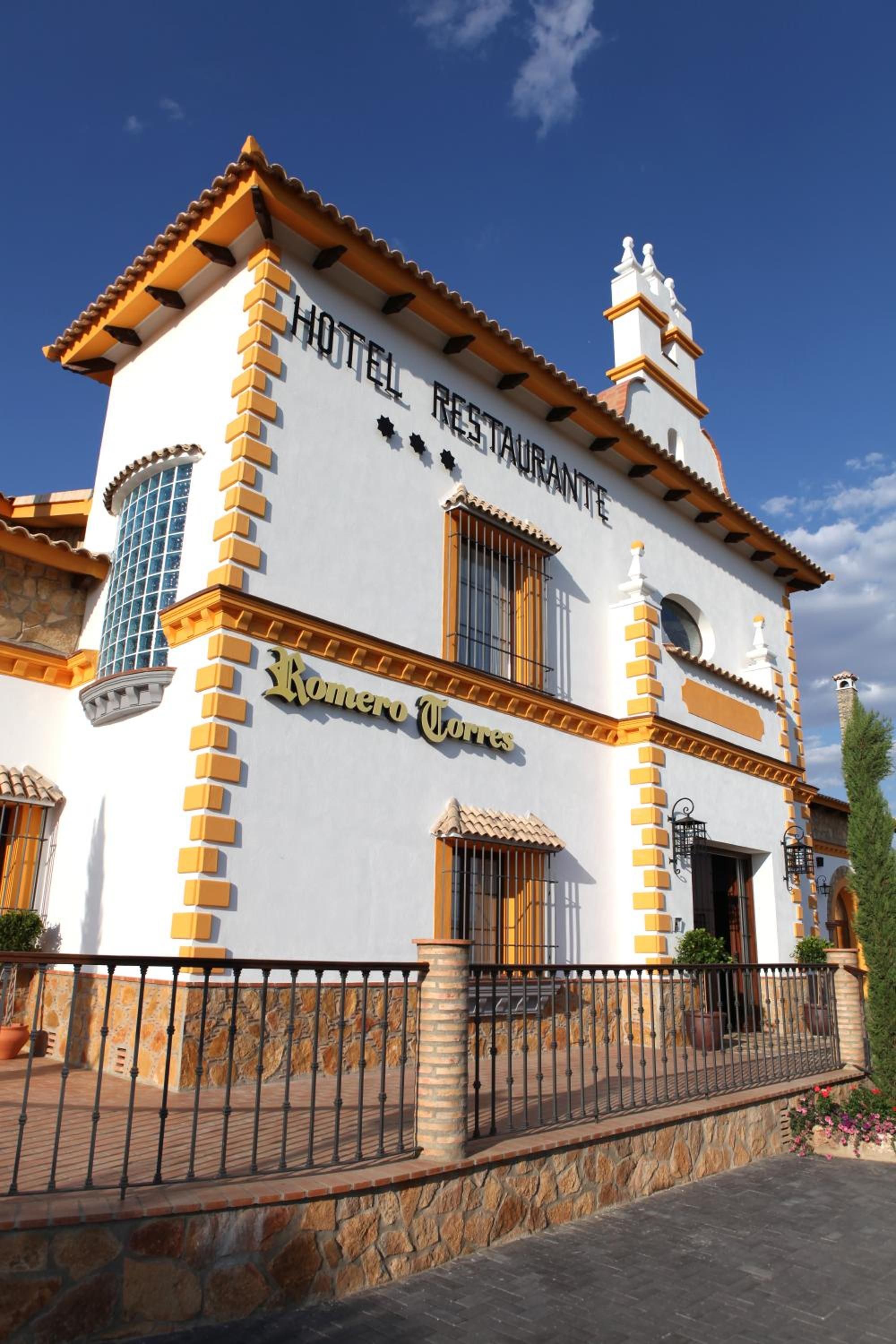 Un hotel con fachada blanca, detalles en amarillo y un letrero que dice 'HOTEL RESTAURANTE'.