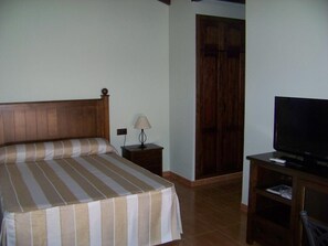 A hotel room with a bed, a nightstand, a lamp, a television, and a wardrobe. - Hotel Rural Romero Torres (Fuente Obejuna)