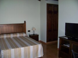 Una habitación de hotel con cama, mesita de noche, lámpara, televisor y armario.