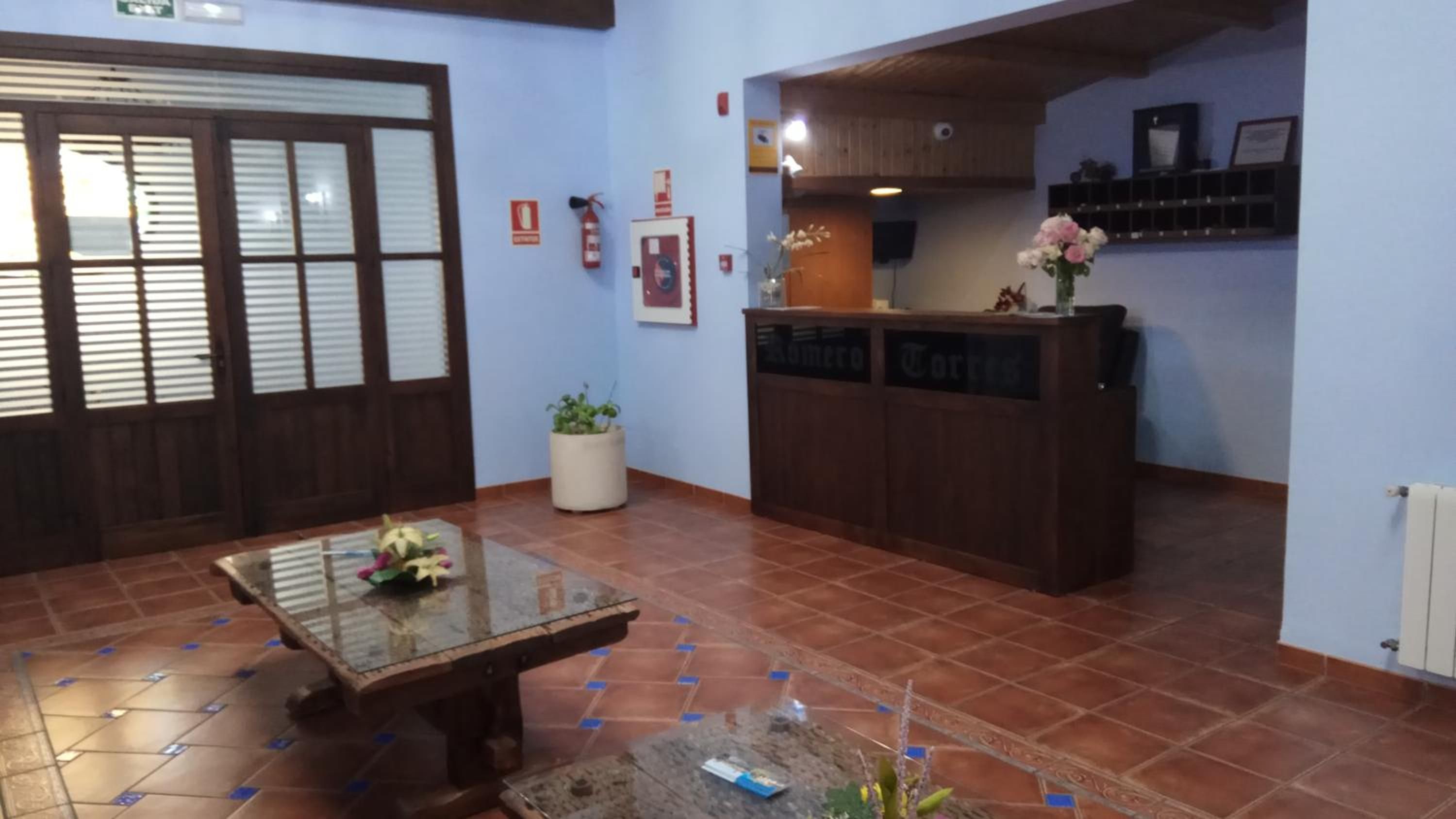 A reception area with a wooden reception desk, a glass-top table with a vase of flowers, a potted plant, and a tiled floor.