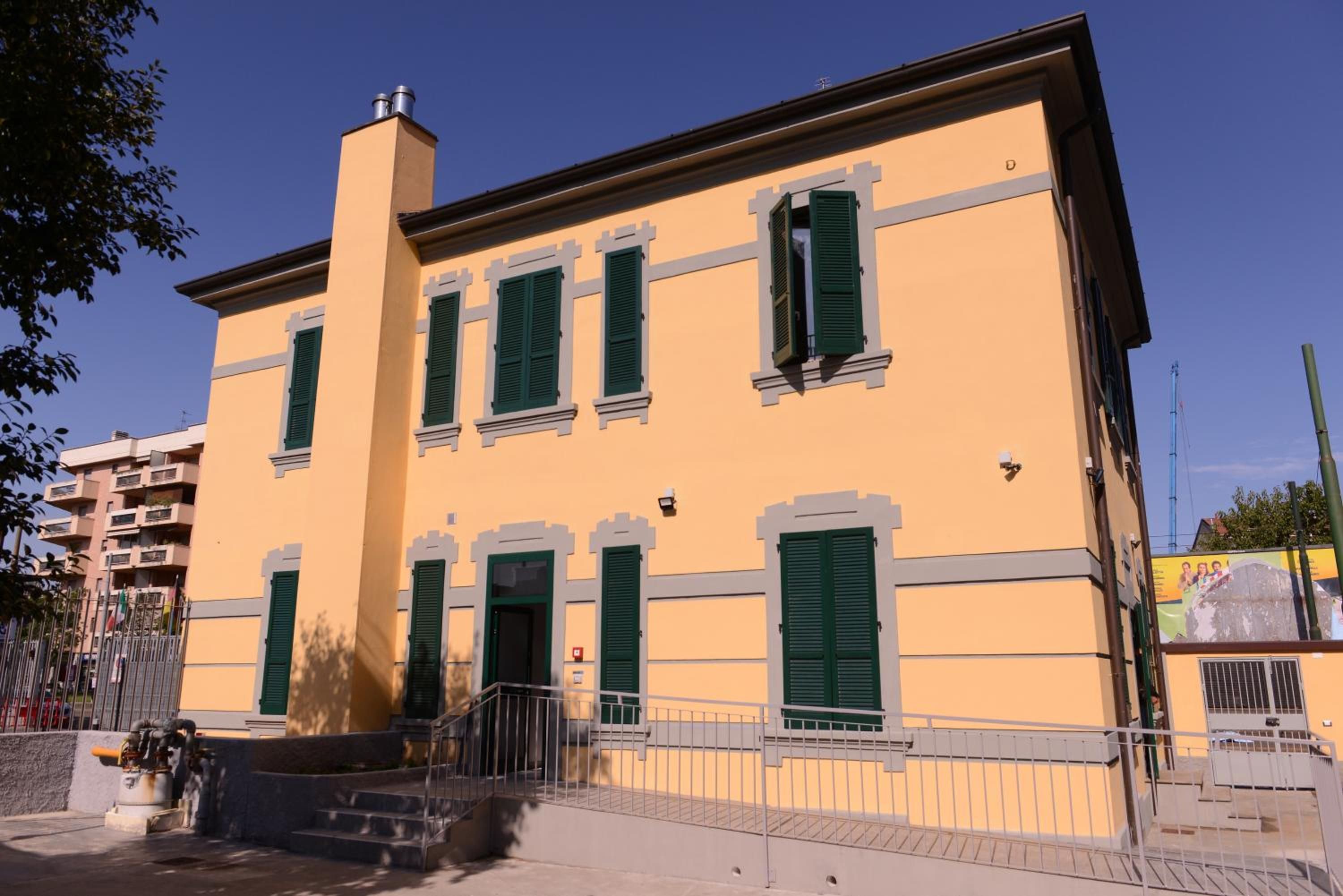 A two-story building with a yellow facade, green shutters, and a central entrance with steps.