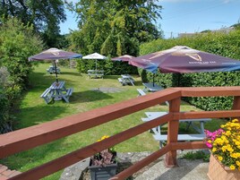 A patio area with picnic tables and umbrellas, surrounded by greenery.