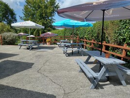 Outdoor picnic tables with umbrellas, surrounded by greenery.