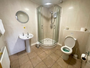 Un baño con ducha envuelta en vidrio, lavamanos pedestal, inodoro y espejo.
