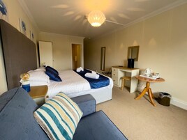 A hotel room with a bed, a desk, a chair, a small table with a kettle, and a trash bin.