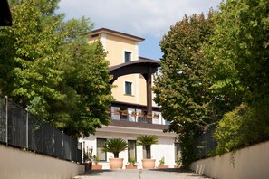 A building with a central archway, surrounded by greenery and a metal fence. - Hotel Barbieri (Altomonte)