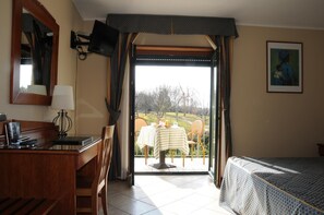 A hotel room with a bed, a desk, a chair, a table with a tablecloth, and a painting on the wall. - Hotel Barbieri (Altomonte)