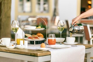 Impostazione colazione con diversi cibi, tra cui croissant, uova e una ciotola di frutta, oltre a diversi bicchieri di bevande.