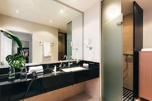 Un bagno moderno con un piano di lavoro nero, due lavabi, un grande specchio e uno spazio doccia.