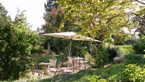 An outdoor seating area with a table and chairs under a large umbrella, surrounded by lush greenery. - Amtshaus Freinsheim (Freinsheim)