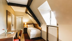 A bedroom with a sloped ceiling, a bed, a desk with a chair, and a radiator. - Amtshaus Freinsheim (Freinsheim)