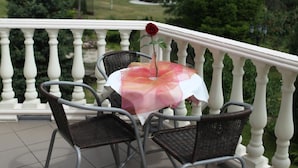 Un patio con una mesa y sillas, una rosa sobre la mesa, y una vista de árboles y un edificio al fondo.