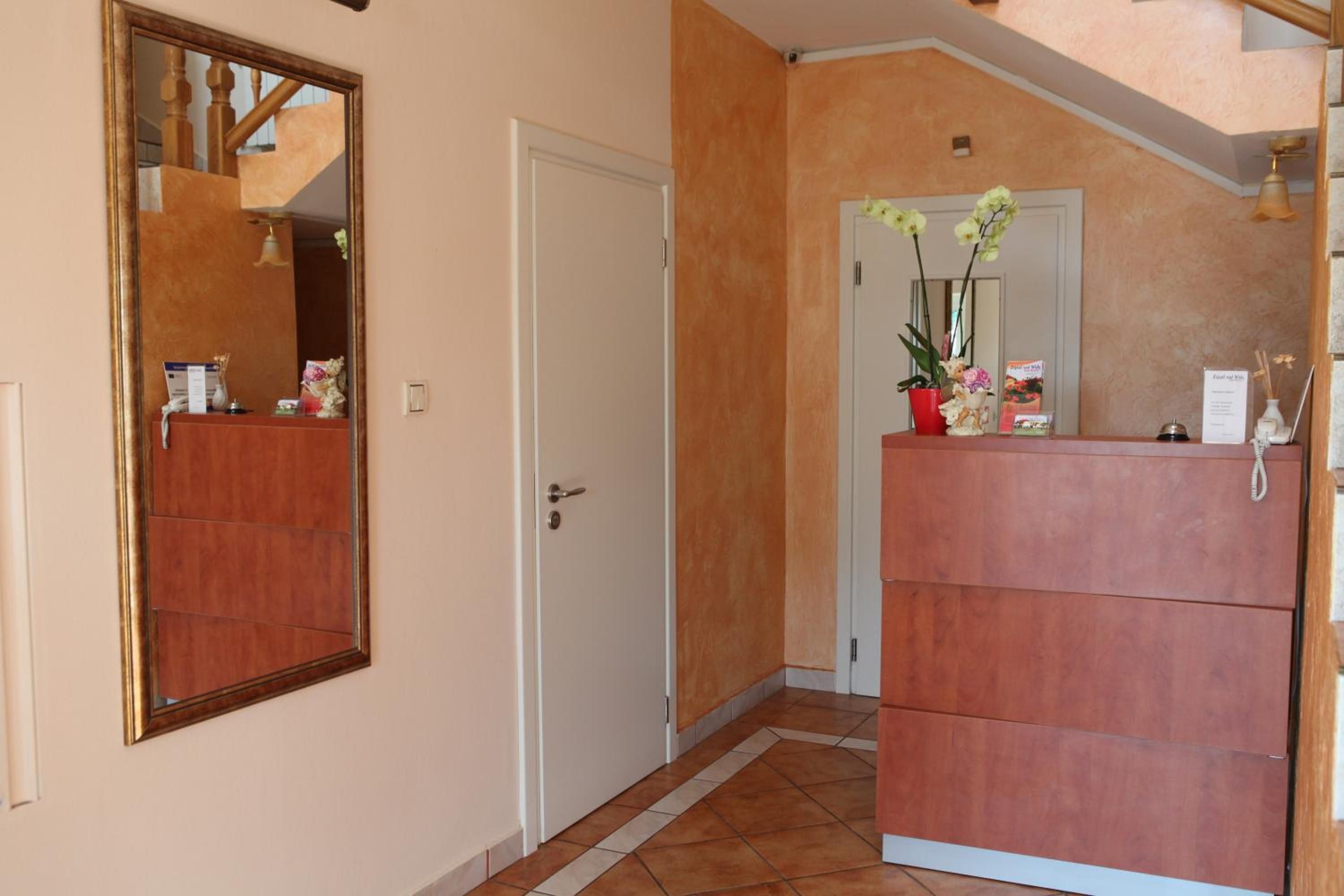 A hallway with a wooden door, a mirror, and a reception desk with a telephone and a vase of flowers.
