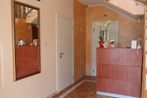 A hallway with a wooden door, a mirror, and a reception desk with a telephone and a vase of flowers.
