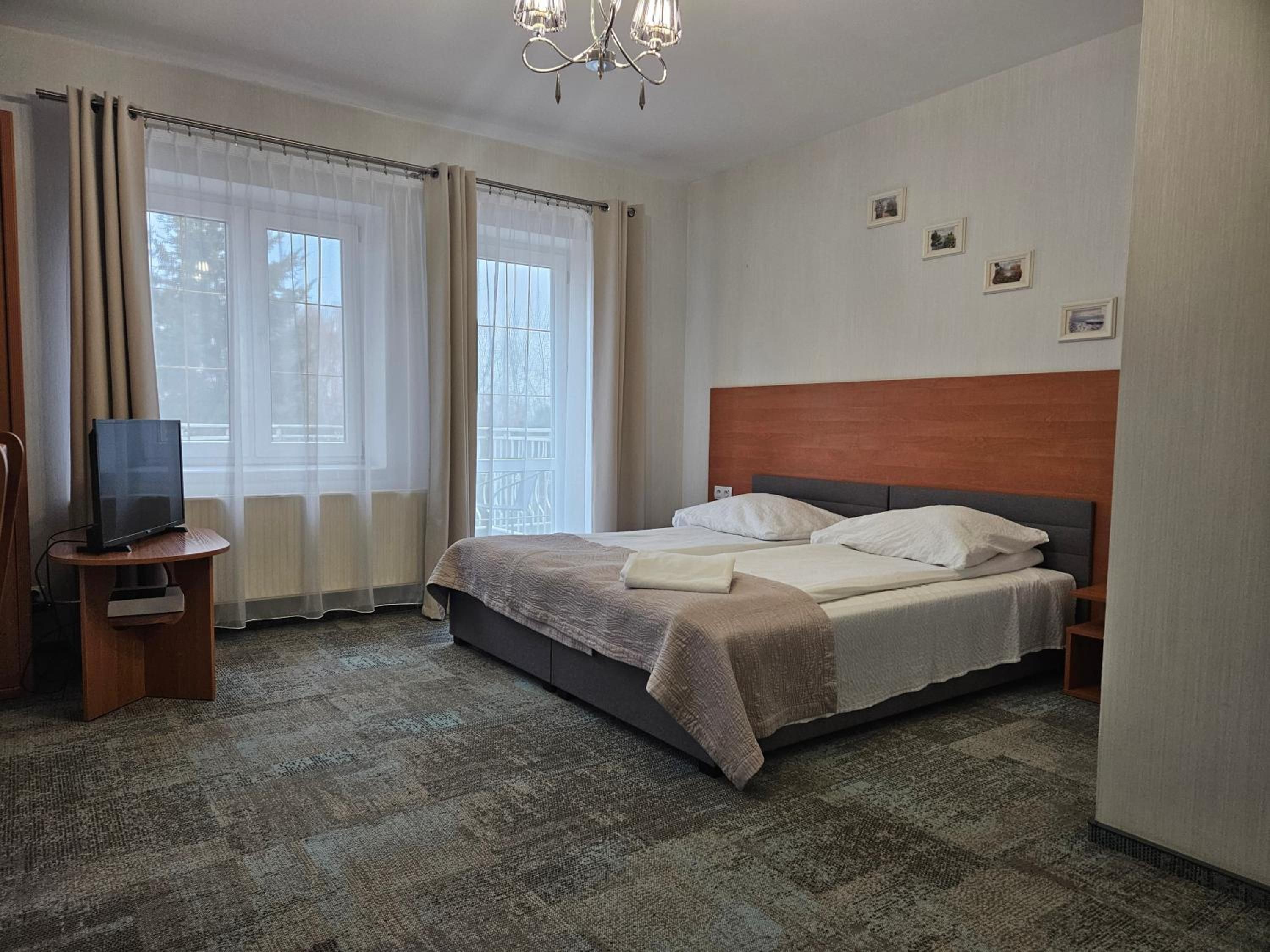 A hotel room with a bed, a television on a stand, and a window with curtains.