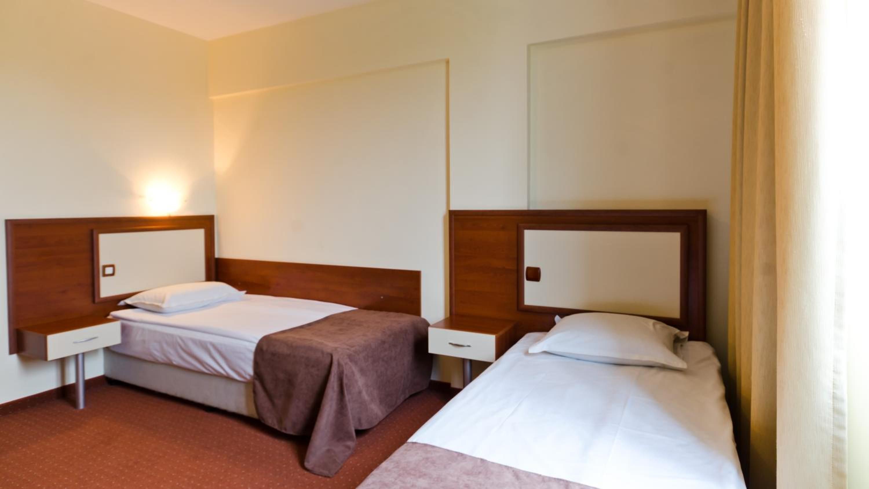 A hotel room with two single beds, each with a wooden headboard and a bedside table.