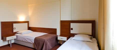 Habitación de hotel con dos camas individuales, cada una con cabecero de madera y mesita de noche.