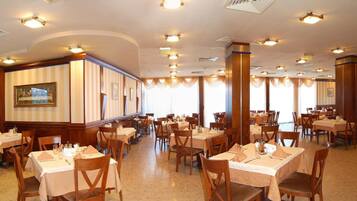 A spacious dining area with multiple tables and chairs, large windows, and a central column.