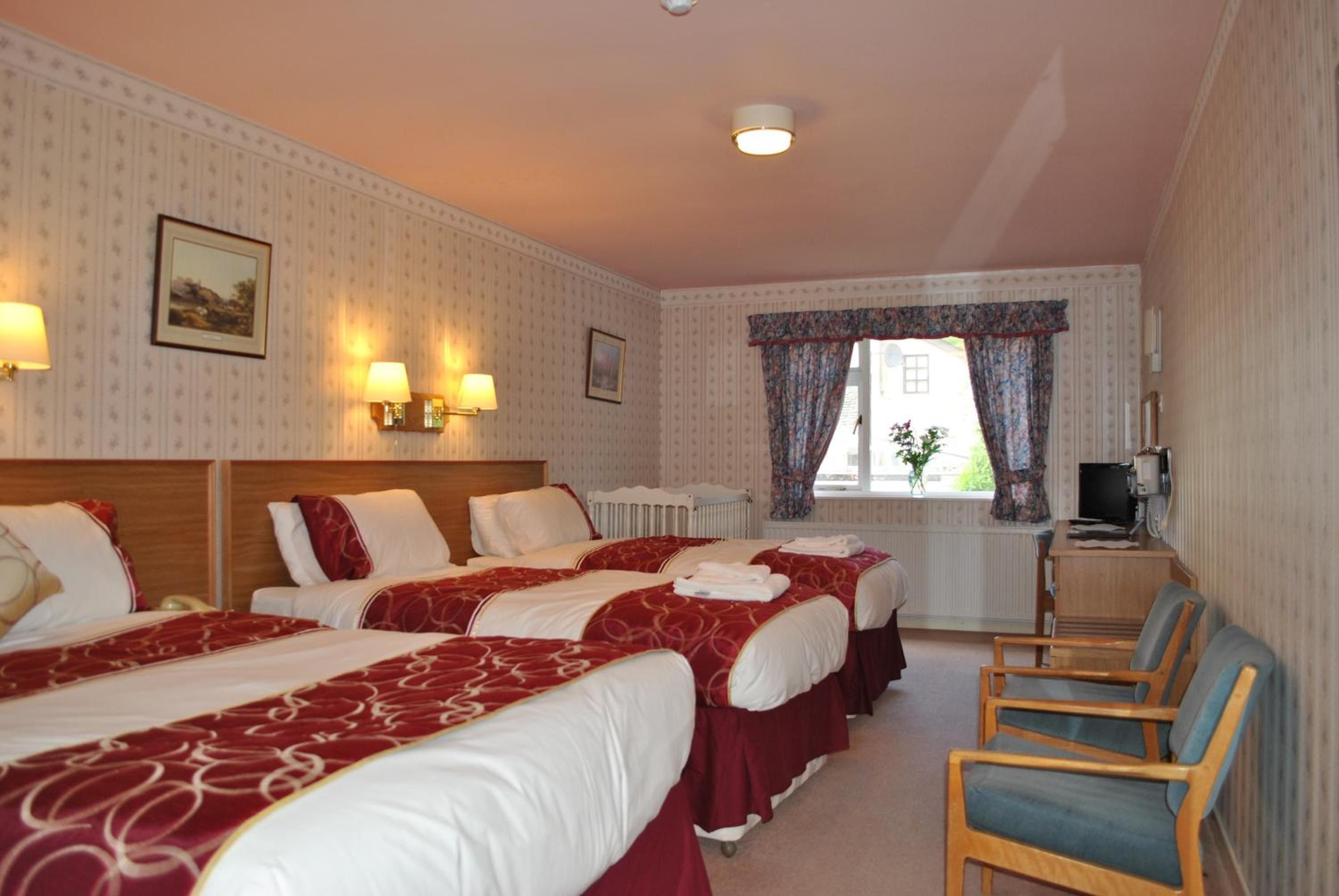 A hotel room with three beds, a desk with a television, and a window with curtains.