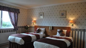 A hotel room with two beds, a window with curtains, wall-mounted lamps, and framed pictures.