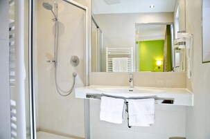 Un baño moderno con cabina de ducha de vidrio, un lavabo blanco y un espejo que refleja una pared verde.