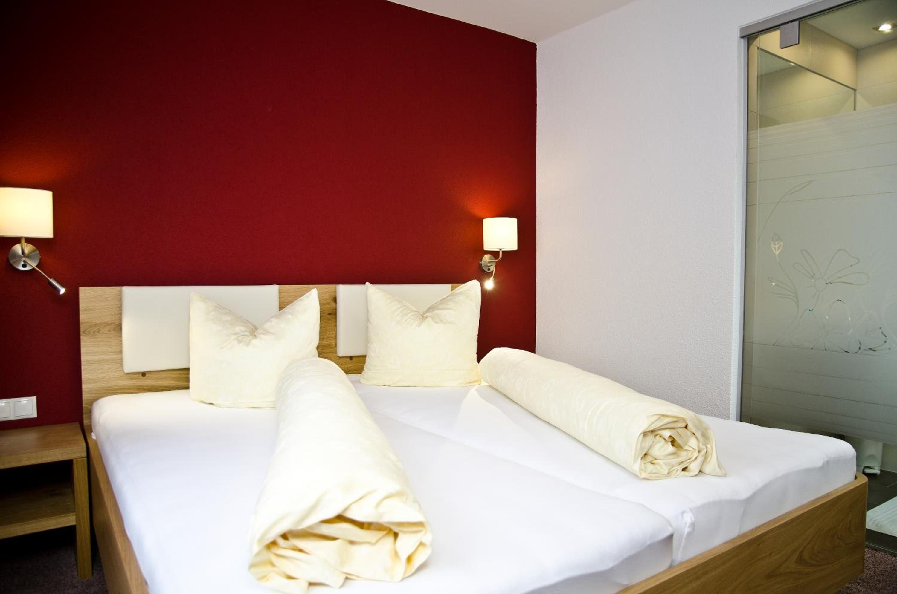 Een hotelkamer met een bed, kussens, een nachtkastje en een wand met een lamp.