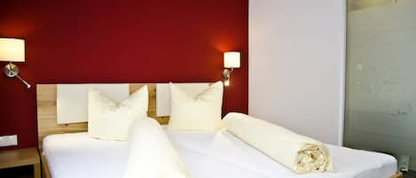 A hotel room with a bed, pillows, a nightstand, and a wall with a light fixture.
