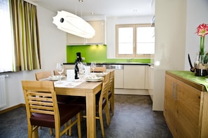 Un comedor con una mesa de madera preparada para cuatro personas, una cafetera y un salpicadero verde en la cocina.