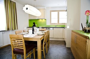 Un comedor con una mesa de madera preparada para cuatro personas, una cafetera y un salpicadero verde en la cocina.