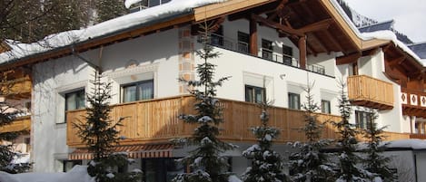 A multi-story building with a wooden facade, balconies, and snow-covered trees.