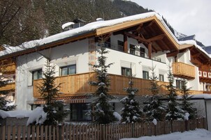 Un edificio de varios pisos con fachada de madera, balcones y árboles cubiertos de nieve.