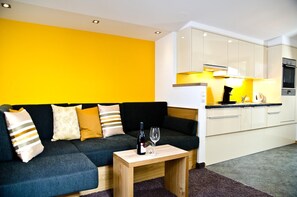 Una sala de estar moderna con un sofá, una mesa de centro y una cocina con armarios y electrodomésticos.