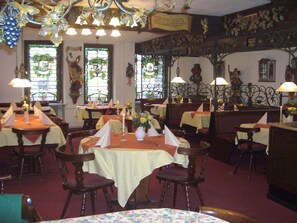 En restauranginteriör med flera matbord, stolar och dekorativa element som till exempel kristallkronor och väggkonst.
