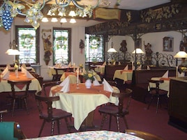 Un interior de restaurante con varias mesas, sillas y elementos decorativos como candelabros y cuadros en las paredes.