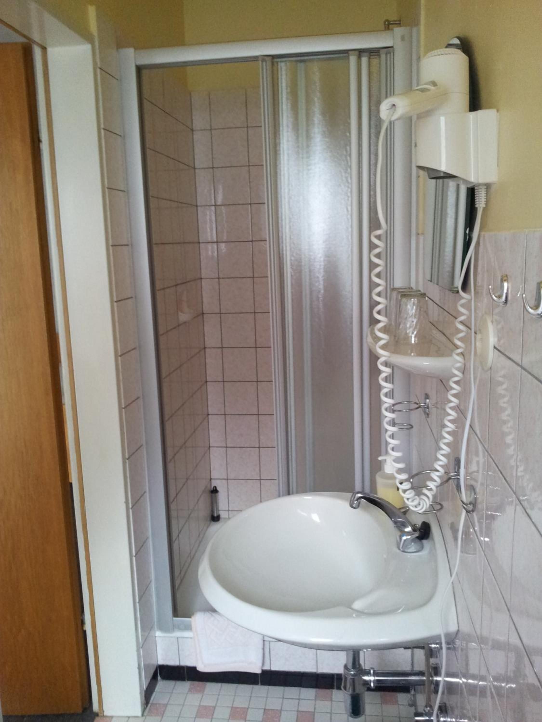 Een badkamer met een douche, een wastafel en een aan de muur bevestigde haardroger.