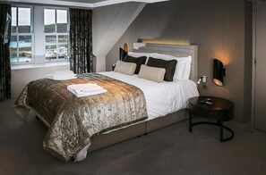Habitación de hotel con cama, mesita de noche, lámpara y vistas al mar a través de amplios ventanales.
