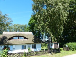 Ein traditionelles Haus mit einem Reetdach, einem umzäunten Hof und einem kleinen Schuppen.